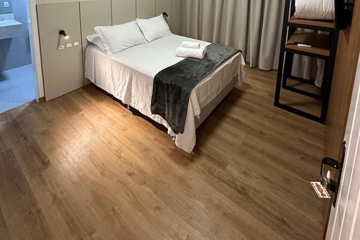 Ett hotellrum med en säng, en inbyggd hylla, en dörr och en taklampa.