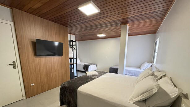 A bedroom with a bed, a TV mounted on the wall, and a wooden ceiling. - HOTEL RIO JORDÃO (Sideropolis)