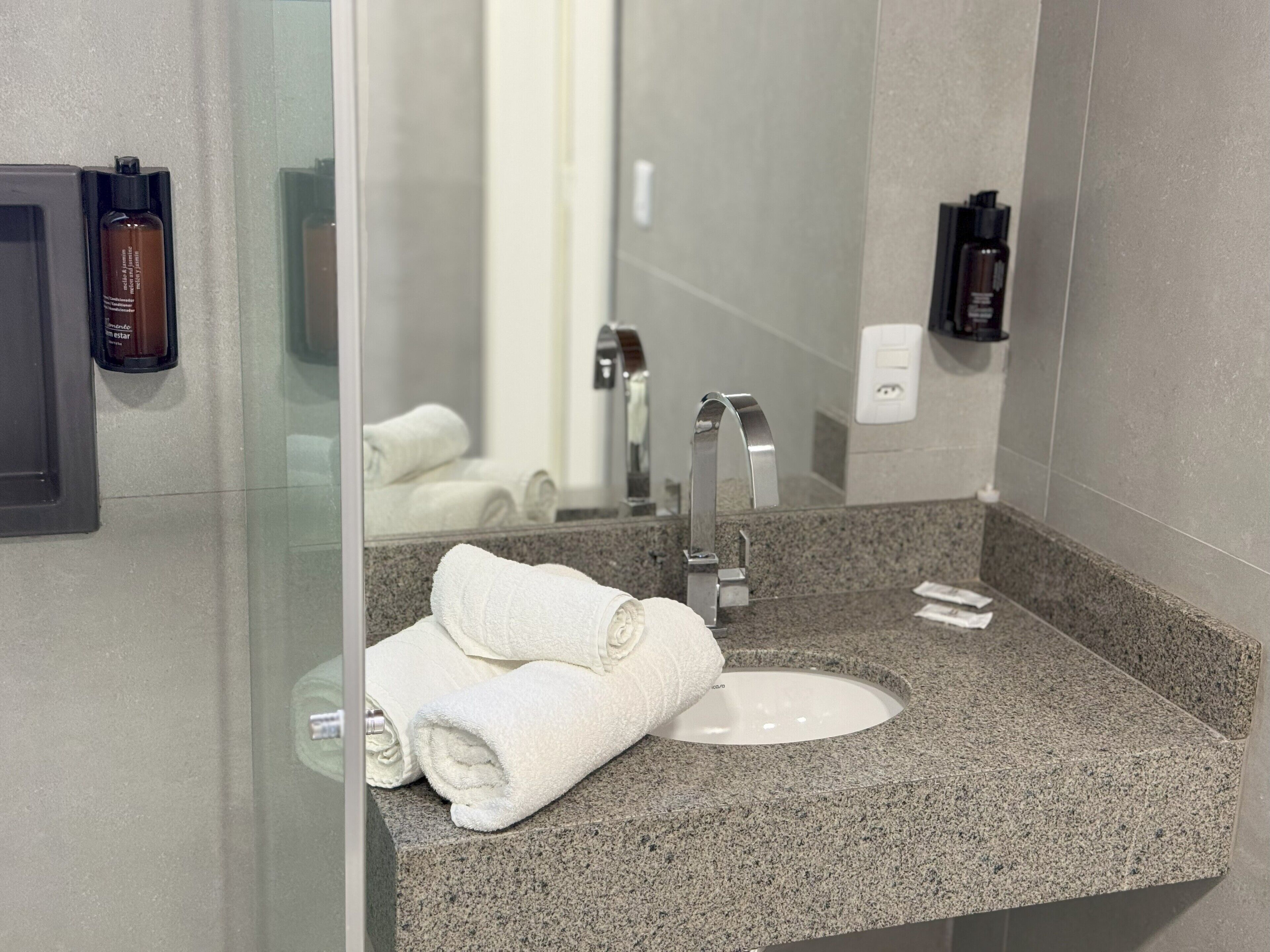 Un baño con encimera de granito, un lavamanos blanco y un espejo. Hay toallas y artículos de aseo en la encimera.