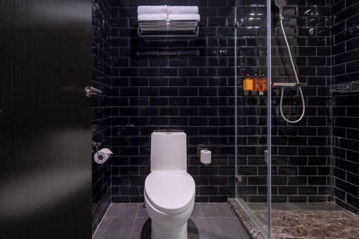 Ein modernes Badezimmer mit schwarzen Fliesenwänden, einer weißen Toilette, einer Duschkabine aus Glas und einem Handtuchhalter über der Toilette.