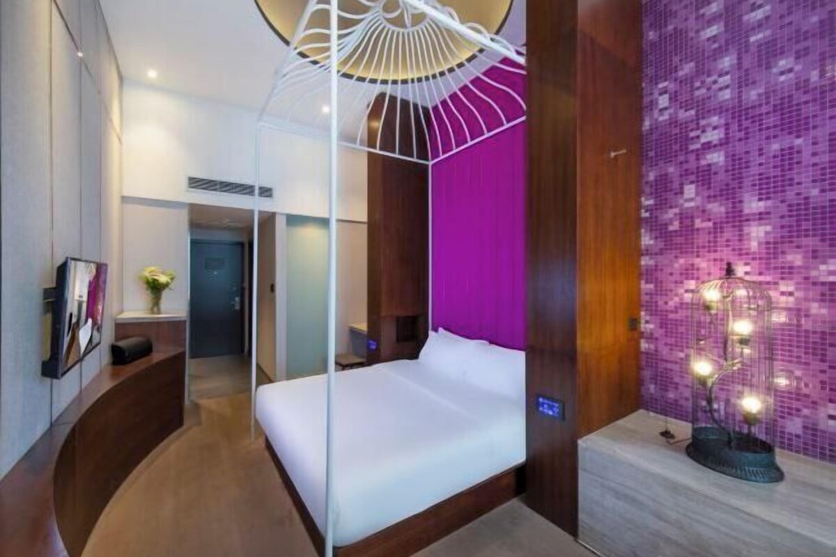 Ein modernes Hotelzimmer mit einem großen Bett, einer außergewöhnlichen Deckenleuchte und einer lebhaften violetten Akzentwand.