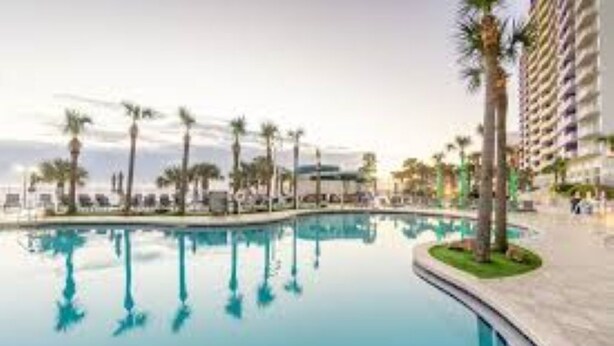 A swimming pool with palm trees and a high-rise building in the background. - 1Bed/1Bath Suite. Daytona Beach, FL! (Daytona Beach)