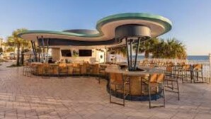 An outdoor seating area with round tables and chairs, a curved structure, and a view of the ocean. - 1Bed/1Bath Suite. Daytona Beach, FL! (Daytona Beach)