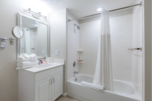Een moderne badkamer met een wit badkamermeubel, een grote spiegel, een bad en een douchegordijn.