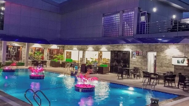 An indoor swimming pool with multiple lanes, surrounded by lounge areas with seating and tables. - VINMILAN Hotel & Resort (Asaba)