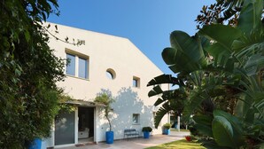 Un edificio moderno con techo plano, ventanas amplias y un patio cubierto con banco y plantas en macetas.