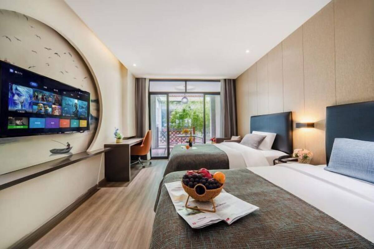 A hotel room with a flat-screen TV, a bed with a headboard, a desk with a chair, and a balcony with a view.