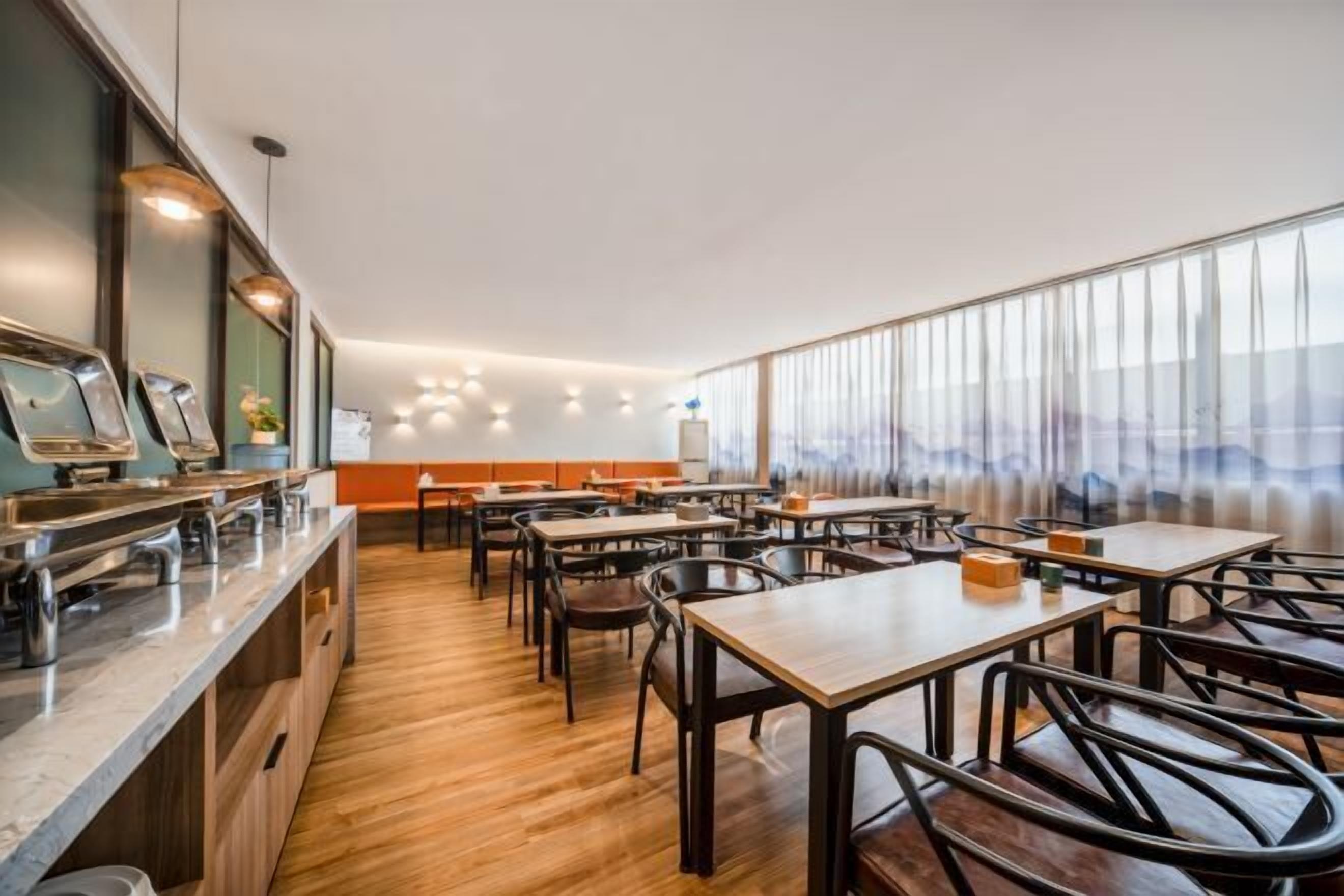 A modern restaurant with wooden tables and chairs, a buffet counter, and large windows offering a view.