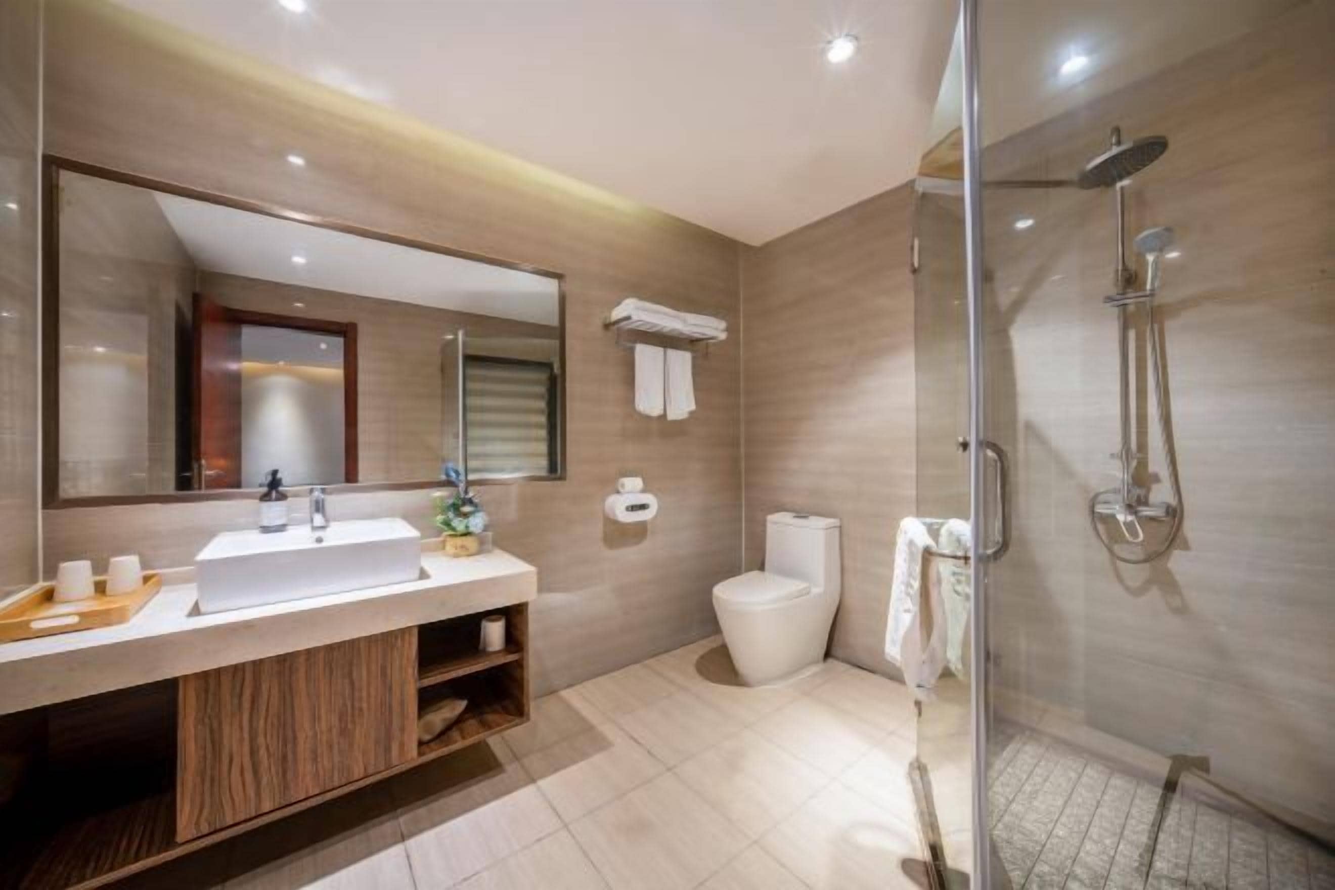 A modern bathroom with a large mirror, a sink, a toilet, and a glass-enclosed shower area.