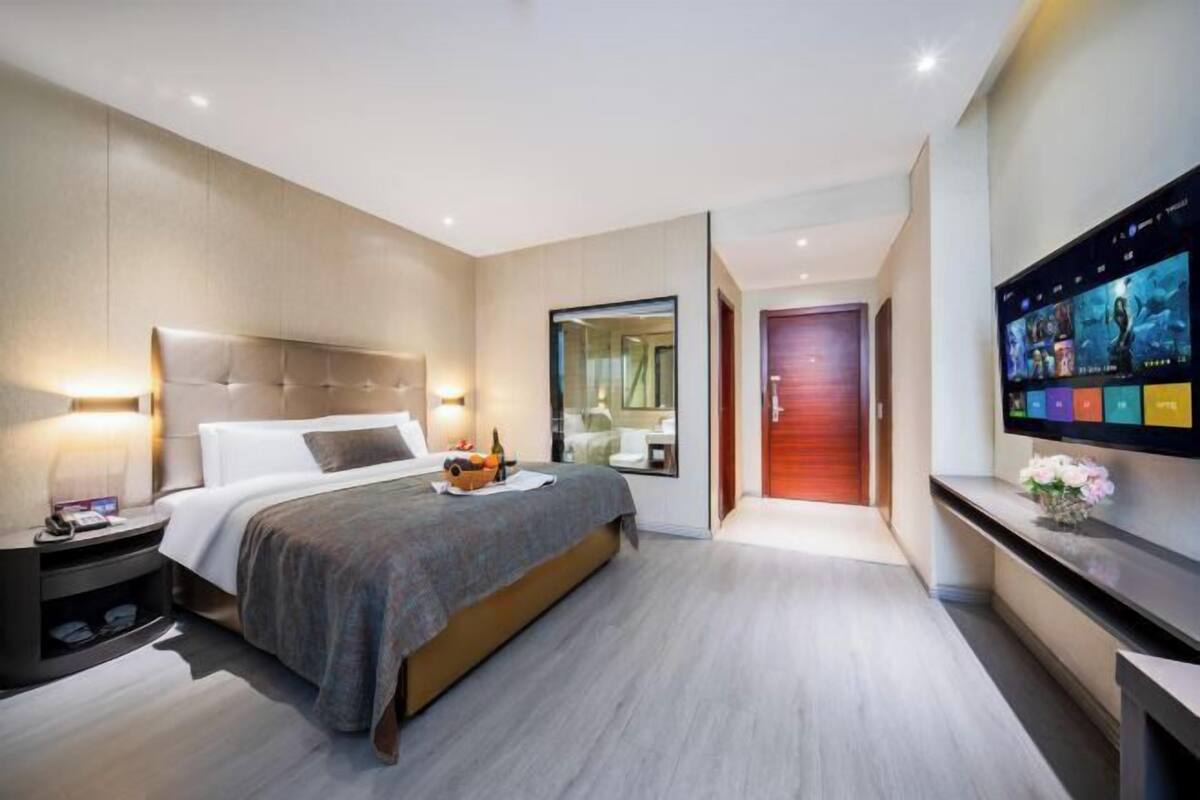A modern hotel room with a large bed, bedside table, and a flat-screen TV mounted on the wall.