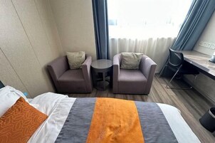 Habitación de hotel con cama, dos sillones, una mesita redonda, escritorio y ventana con cortinas.
