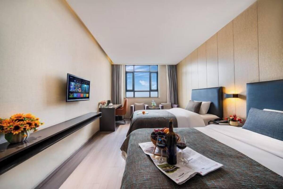 A hotel room with two beds, a desk, a TV, and a window with curtains.