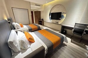 A hotel room with two beds, a TV mounted on the wall, a mirror, and a small seating area.