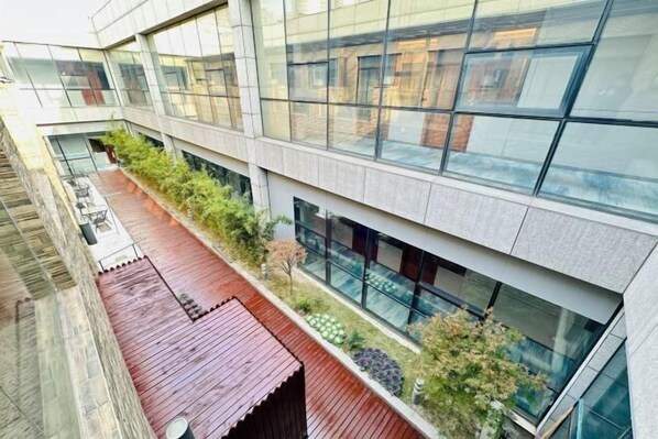 A modern building with a glass facade, a wooden deck, and a landscaped area with plants.