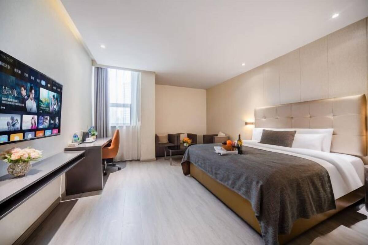 A modern hotel room with a bed, desk, chair, TV, and a window.