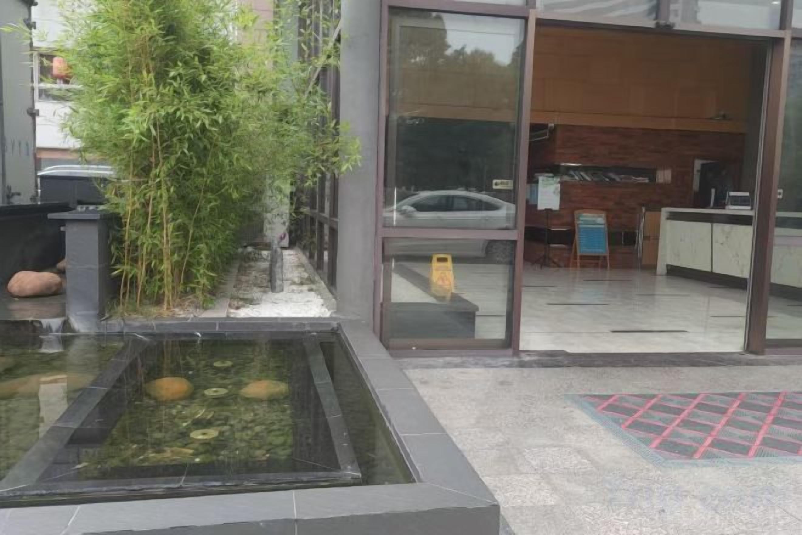A reception area with a reception desk, a car parked outside, and a water feature with plants.