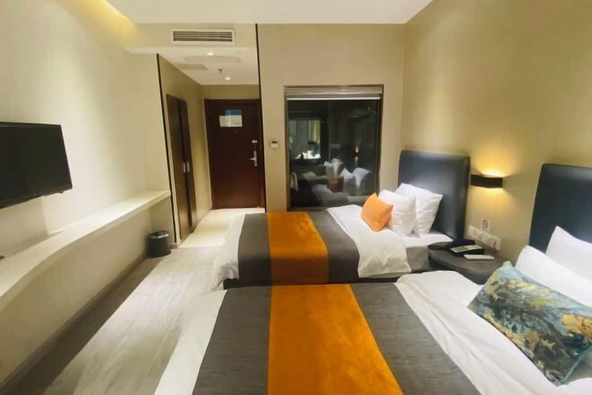 Ein Hotelzimmer mit zwei Betten, einem Fernseher, einem Nachttisch und einer Badezimmertür.