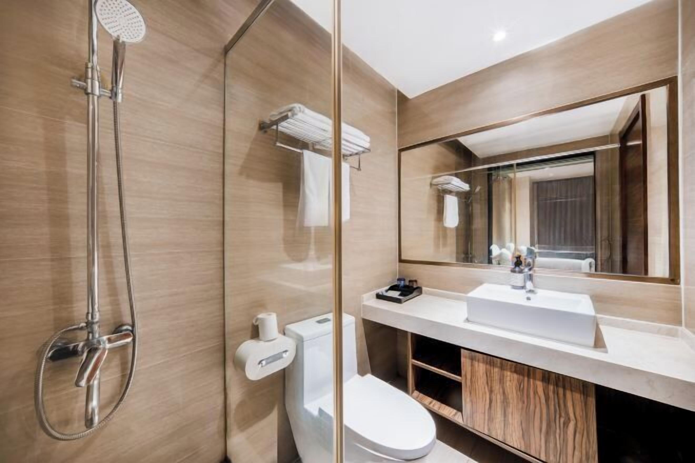 A modern bathroom with a glass shower enclosure, a white toilet, a large mirror, and a wooden vanity.