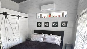 A bedroom with a bed, a ceiling fan, a window, and a shelf with decorative items. - Cozy hot tub cabin in charming Scaly Mountain, what a gem! (Scaly Mountain)
