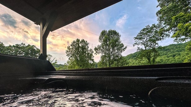A view from a train window with water on the tracks, a bridge overhead, and green trees in the background. - Cozy hot tub cabin in charming Scaly Mountain, what a gem! (Scaly Mountain)