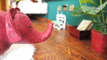 A toy elephant on a wooden floor with a potted plant and a small white object in the background.
