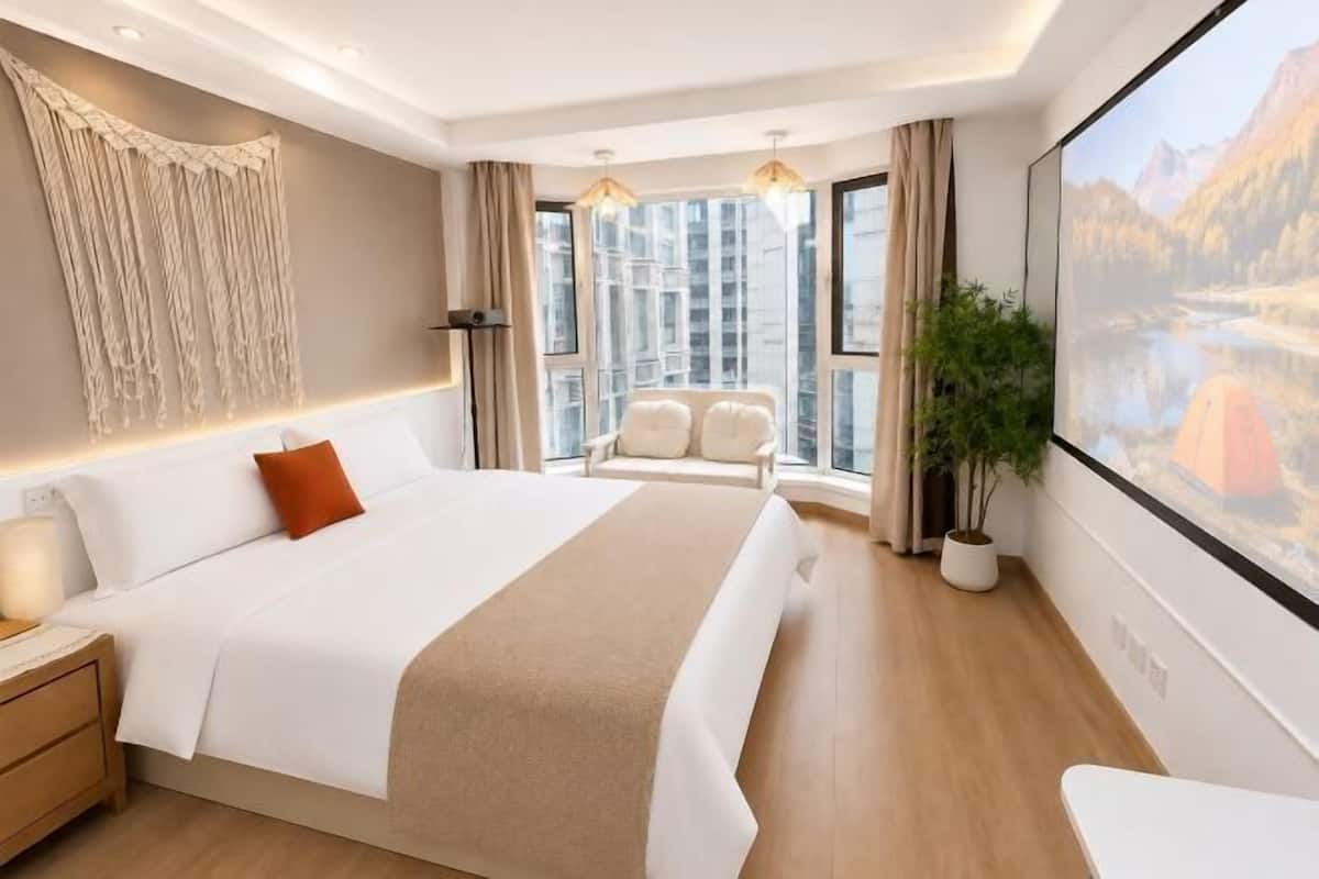 Une chambre d’hôtel avec un grand lit, une table de chevet, une chaise, une grande fenêtre donnant sur la montagne et une plante.