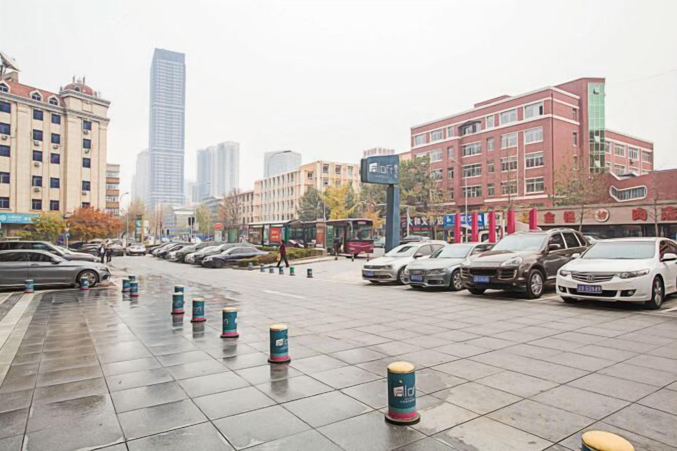 A city street with parked cars, buildings, and bollards.