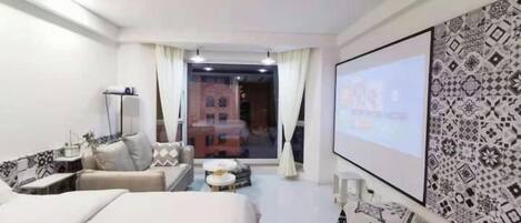 Quarto de hotel com cama, sofá, mesa pequena e tela de TV.