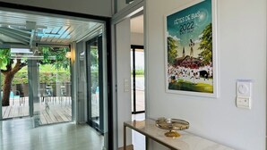A modern hotel lobby with a glass door leading to an outdoor patio, a framed poster on the wall, and a marble-topped reception desk.