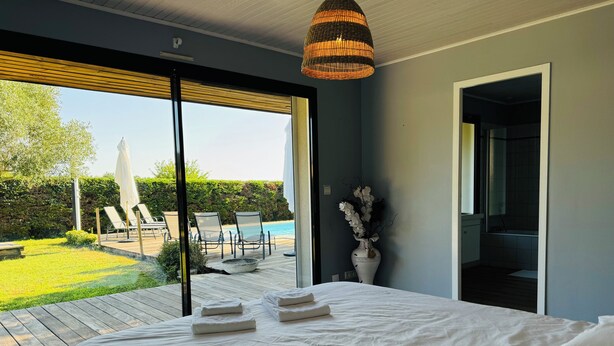 A bedroom with a large bed, a view of a pool and outdoor chairs, and a vase with flowers.