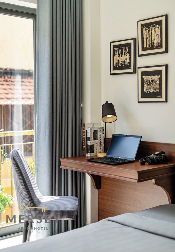 Une chambre d’hôtel équipée d’un bureau, d’un ordinateur portable, d’un appareil photo et d’une œuvre d’art encadrée accrochée au mur.