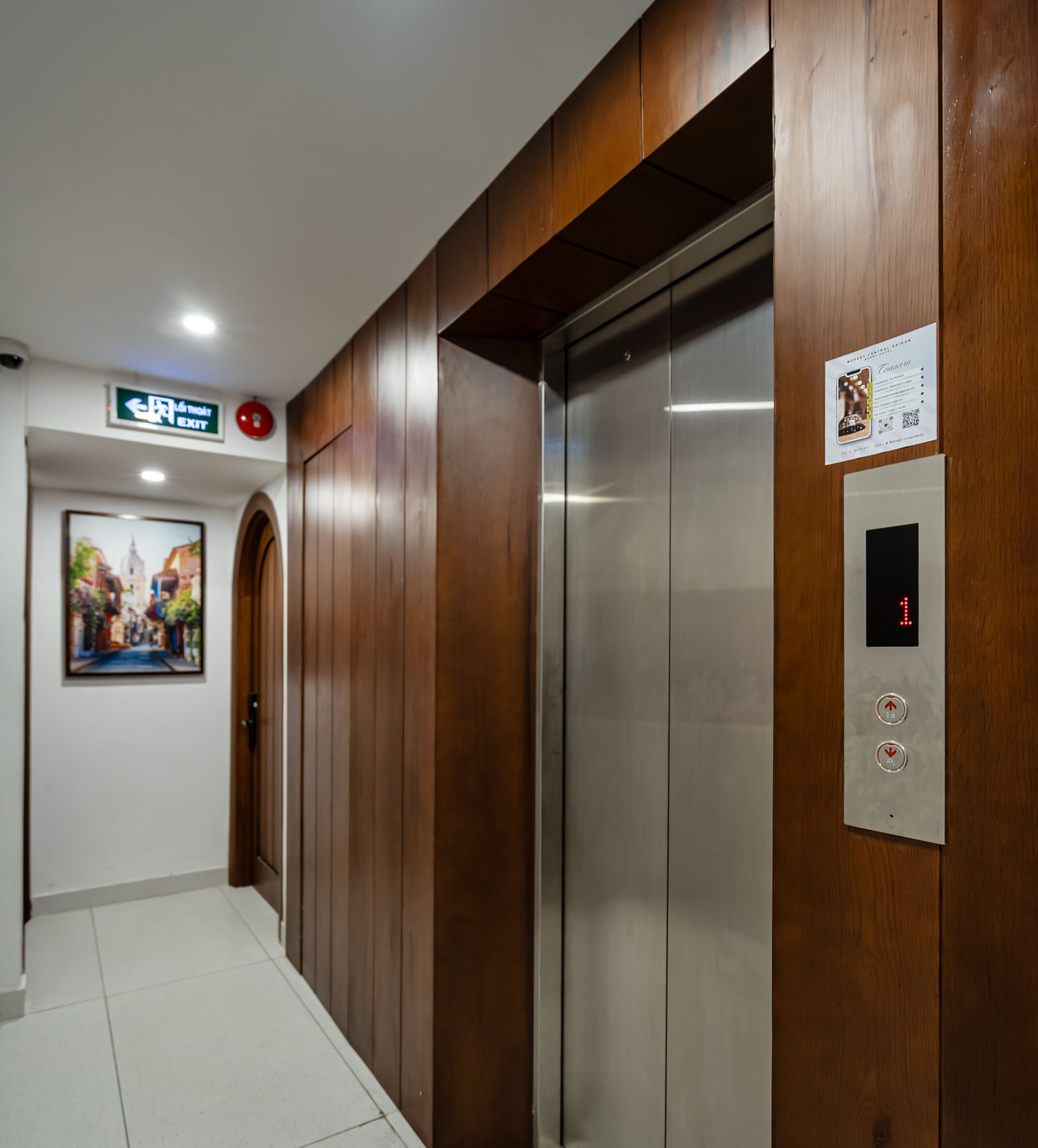 An elevator with a control panel, a sign indicating an exit, and a framed picture on the wall.