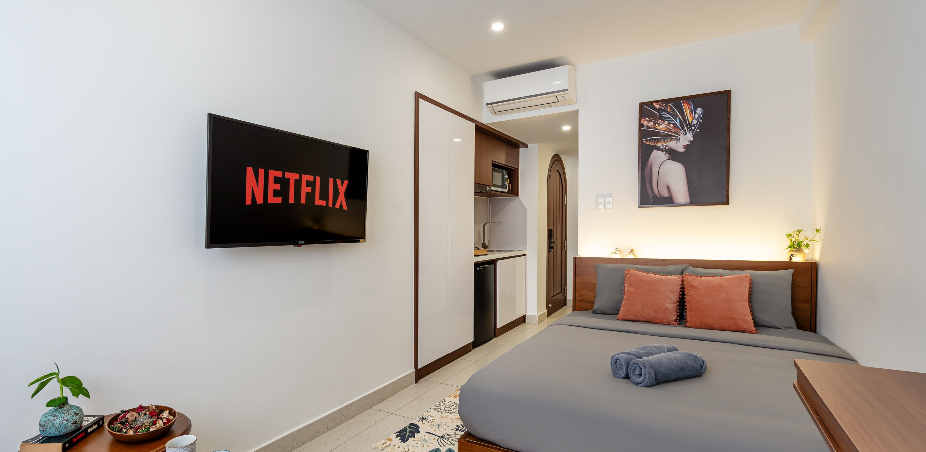 Une chambre d’hôtel moderne équipée d’un lit, d’un téléviseur affichant l’interface de « NETFLIX », d’une petite kitchenette et d’un tableau au mur.