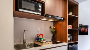 Een moderne keuken met een magnetron, gootsteen en inbouwkeuken. Een klein plankje met snacks en een plantje is te zien. Een zwarte vaatwasser is rechts zichtbaar.