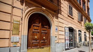 Un bâtiment doté d’une grande porte double en bois, d’un petit espace extérieur aménagé pour s’asseoir et d’un arbre situé sur la droite.