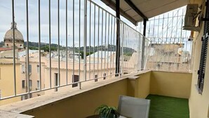 Un balcon donnant sur un dôme et des bâtiments, une petite table avec des chaises et un revêtement de sol vert artificiel.