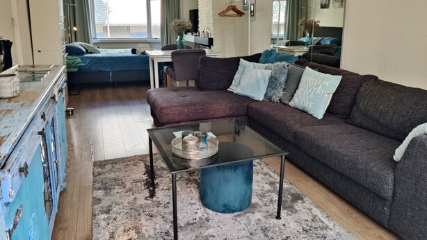 A living room with a sofa, a glass coffee table, a dresser, and a bed. - Stylish Lottus Room in Duplex Near Center & UMCG (Groningen)