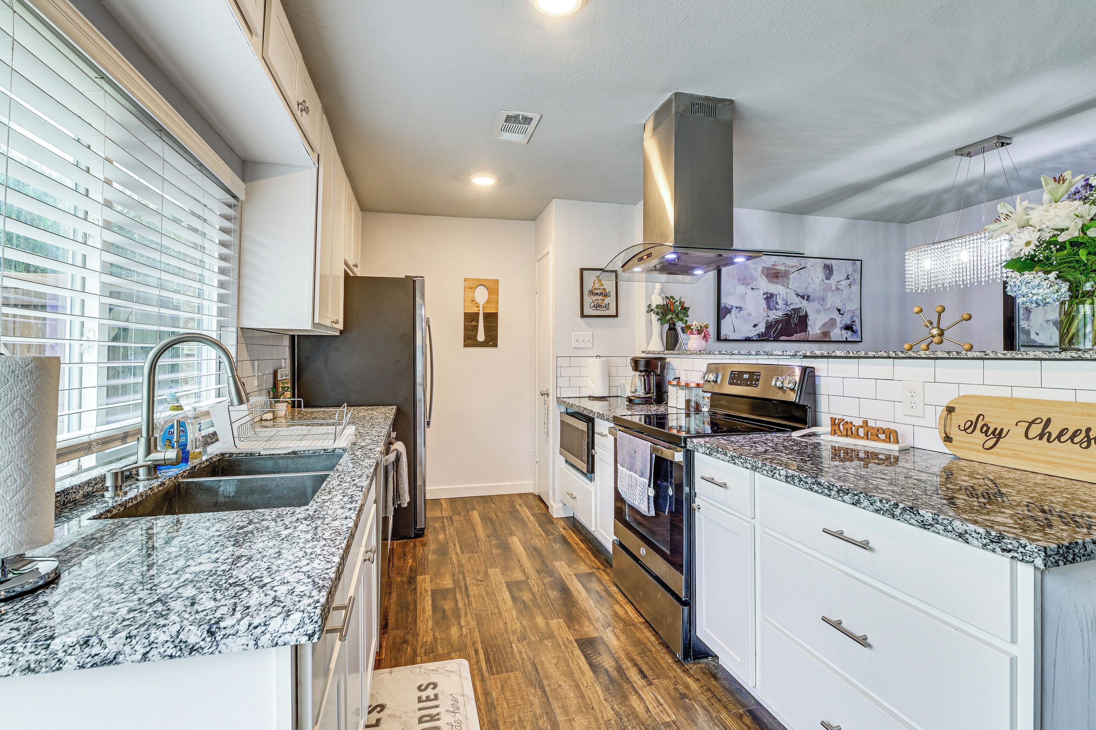 A modern kitchen with white cabinets, granite countertops, a stainless steel range hood, and a built-in oven.