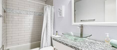 A bathroom with a glass sink, white toilet, and a shower with a white curtain.