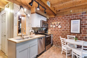 Una cocina con pared de ladrillo, electrodomésticos de acero inoxidable y un comedor con sillas blancas.