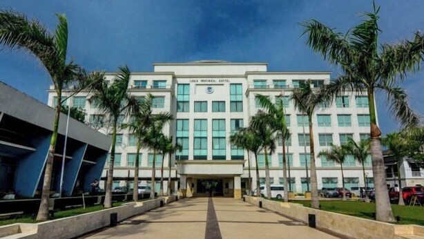 A modern building with a central entrance, surrounded by palm trees and a paved walkway.