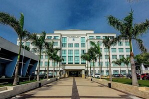 Un edificio moderno con entrada central, rodeado de palmeras y un camino pavimentado.