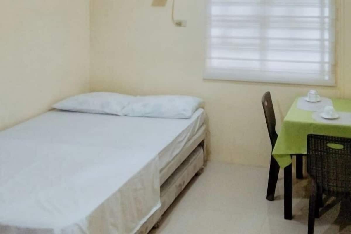 A small room with a single bed, a table with a green tablecloth, and a chair.