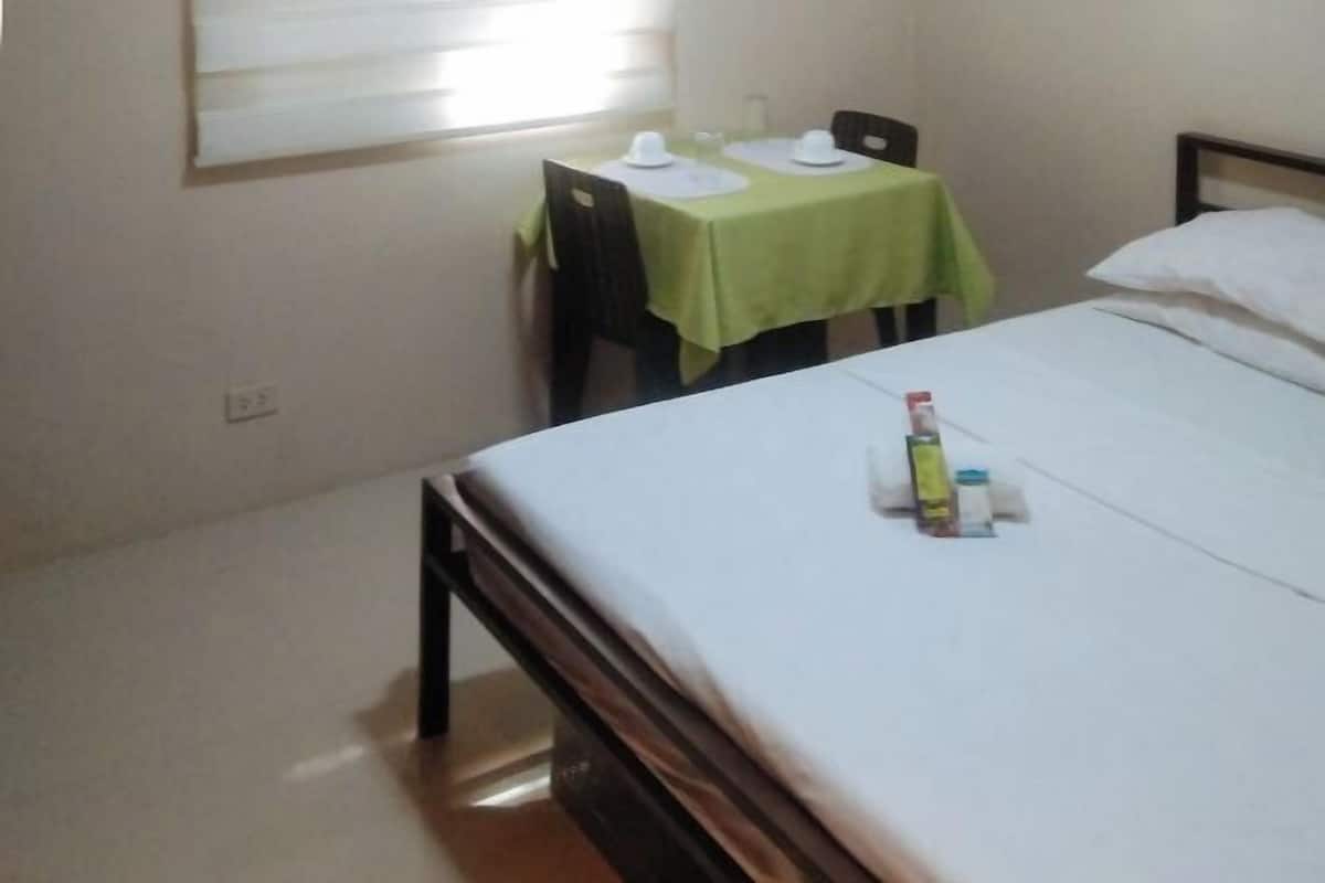 A room with a bed, a table with a green tablecloth, and a window with blinds.