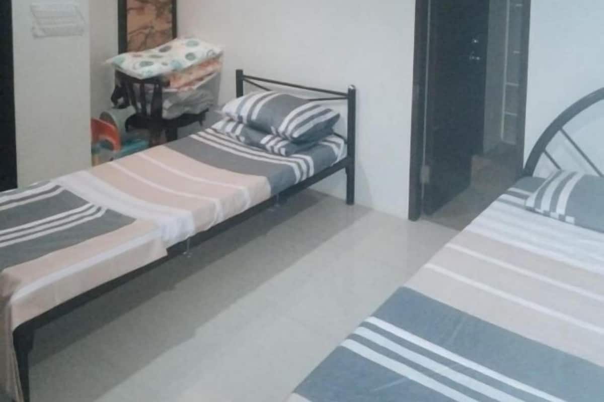A single bed with striped bedding, a small table with a patterned tablecloth, and a chair.