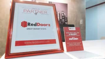 A framed sign with RedDoorz branding, a website URL, and a contact number.
