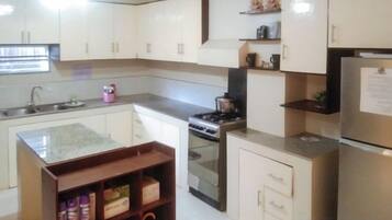 A kitchen with white cabinets, a stainless steel refrigerator, a built-in oven, and a wooden shelf with jars.