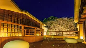 Un bâtiment traditionnel japonais doté d’une terrasse en bois, de grandes fenêtres et offrant une vue sur un arbre.