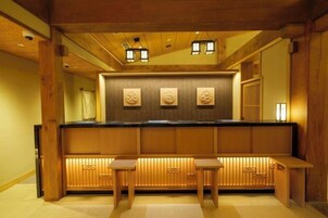 A traditional Japanese-style room with a wooden reception desk, two wooden stools, and a wall with carved panels.