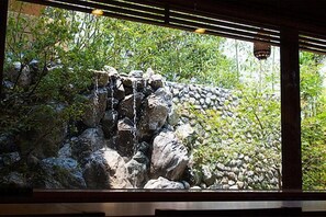 A view through a window of a stone wall with a small waterfall, surrounded by greenery.